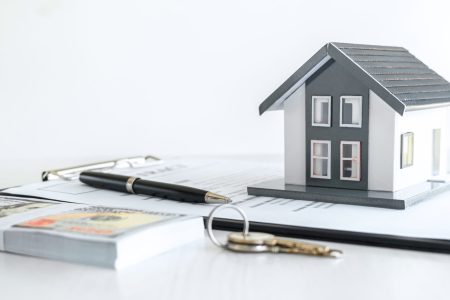 House model and Money, house key lying on real estate contract, home loan and investment concept.